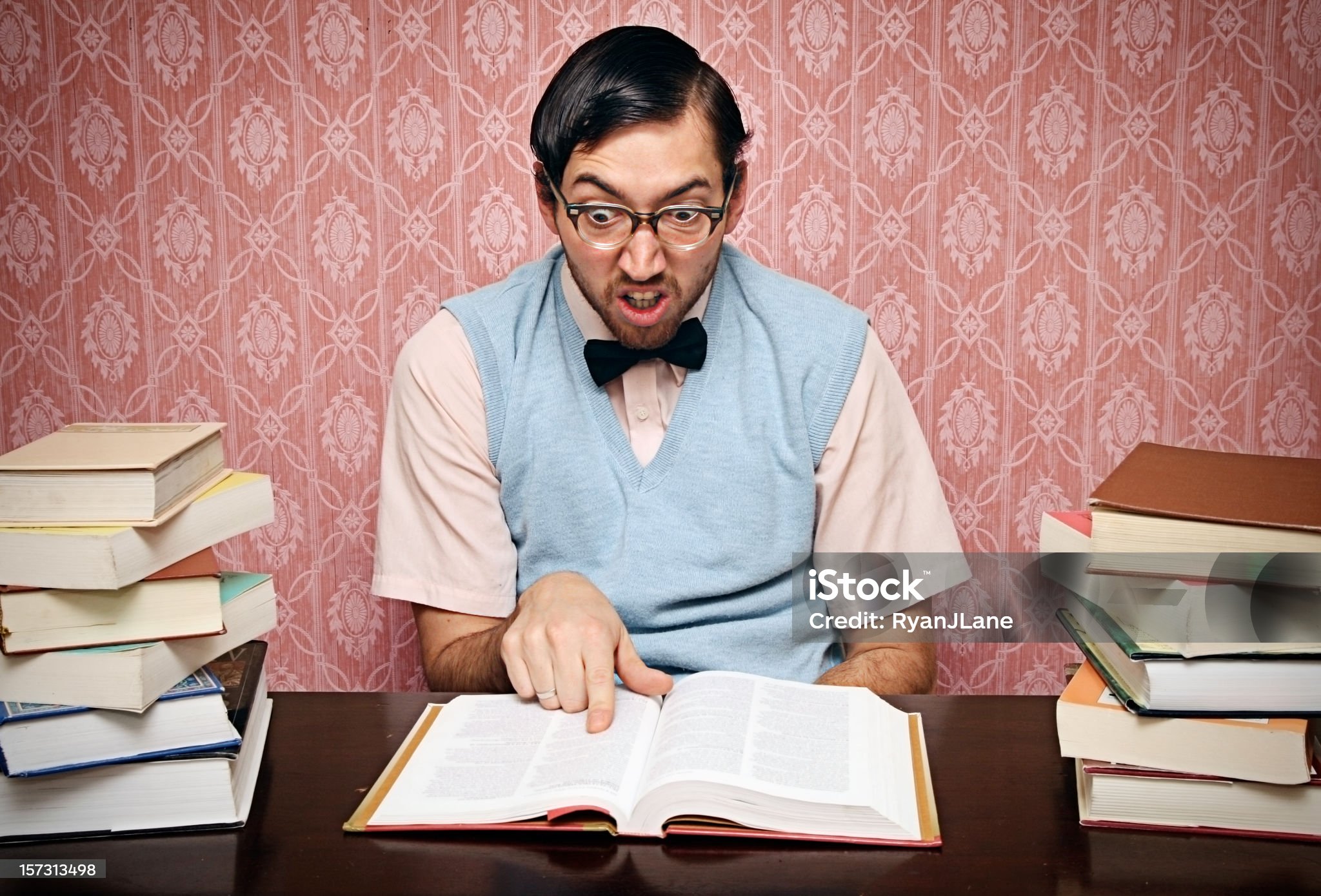 Nerdy young man concentrates intently on his school text book. Horizontal with copy space.